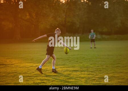 Ein muskeliger Teenager spielt bei Sonnenuntergang in einem Londoner Park Rugby Stockfoto