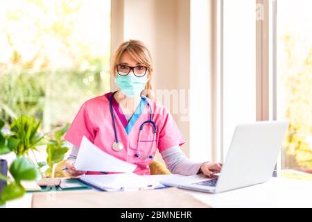 Porträtaufnahme einer Ärztin, die eine Gesichtsmaske zur Vorbeugung trägt, während sie im Krankenhaus am Laptop arbeitet. Stockfoto