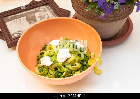 Zucchini Spaghetti mit Erbsen und Ricotta in natürlichem Licht mit einer schönen Pflanze mit lila Blüten und zwei kleine Plätze in der Nähe Stockfoto