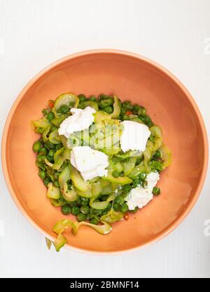 Zucchini Spaghetti mit Erbsen und Ricotta in natürlichem Licht mit einer schönen Pflanze mit lila Blüten und zwei kleine Plätze in der Nähe Stockfoto