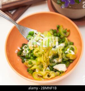 Zucchini Spaghetti mit Erbsen und Ricotta in natürlichem Licht mit einer schönen Pflanze mit lila Blüten und zwei kleine Plätze in der Nähe Stockfoto