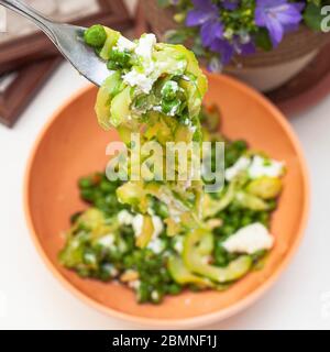 Zucchini Spaghetti mit Erbsen und Ricotta in natürlichem Licht mit einer schönen Pflanze mit lila Blüten und zwei kleine Plätze in der Nähe Stockfoto