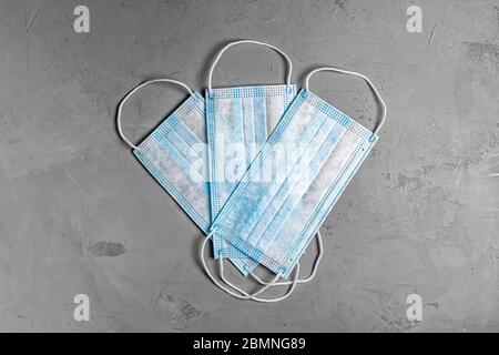 Drei blaue Einwegmaske auf grauem Betongrund. Flaches Lay. Draufsicht Stockfoto