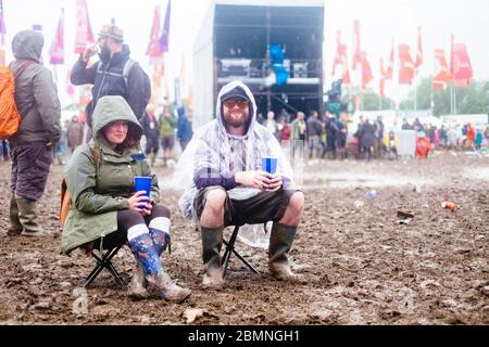 Ein Paar, auf Stühlen, im Schlamm mit Regenmänteln und wellington-Stiefeln auf dem Glastonbury Festival 2016 – Bilddatum Sonntag, 26. Juni 2016 (Pilton, so Stockfoto