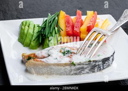 Lachssteak mit cremiger Sauce und gemischtem Gemüse auf schwarzem Steingrund Stockfoto