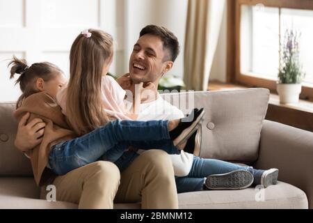 Glücklicher Vater spielt mit zwei Töchtern, kitzelt auf der Couch Stockfoto