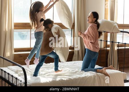 Glückliche Mutter spielt Kissenkampf mit zwei kleinen Töchtern Stockfoto
