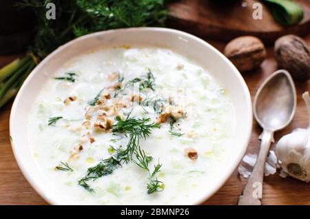 Bulgarische Joghurt kalte Suppe Tarator - mit Joghurt, Gurken, Knoblauch, Olivenöl, Dill und Walnüsse. In einem Keramikbecher mit einem alten Löffel angeordnet Stockfoto