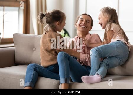 Glückliche Mutter spielt mit kleinen Töchtern, kitzelt auf der Couch Stockfoto