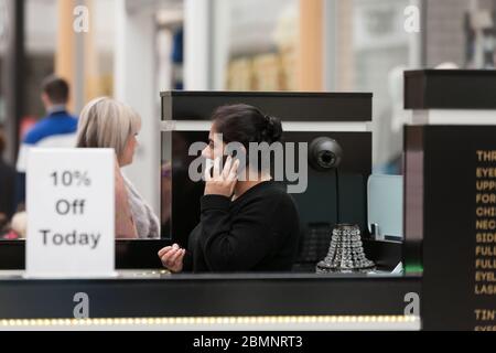 HUDDERSFIERLD, WEST YORKSHIRE, Großbritannien - MÄRZ 21: Ein Nageltierhelfer mit Gesichtsmaske spricht auf einem Handy im Kingsgate Shopping Centre, Huddersfield Stockfoto