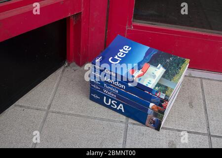 Ein kleiner, netter Haufen gebrauchter Reiseführer von Lonely Planet (Kreta, London, Tunesien, Wales, USA), die vor der Haustür eines Charity-Shops liegen. Stockfoto