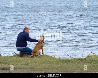 Ein Mann streichelte seinen Hund in der Nähe des Sees. Freundschaft und Liebe für Haustiere Konzept. Stockfoto