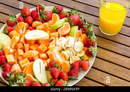 Teller mit Auswahl an Obstscheiben auf einem Holztisch und Glas mit frischem Orangensaft gesundes Esskonzept Stockfoto