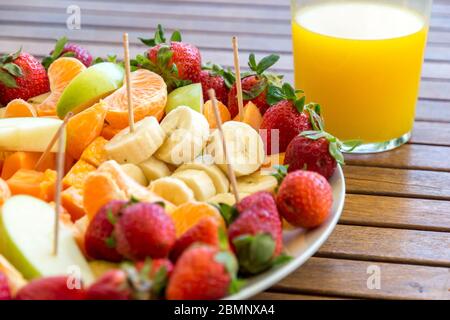 Teller mit Auswahl an Obstscheiben auf einem Holztisch und Glas mit frischem Orangensaft gesundes Esskonzept Stockfoto