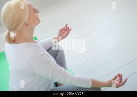 Reife blonde Frau sitzt in Lotushaltung, meditieren Stockfoto