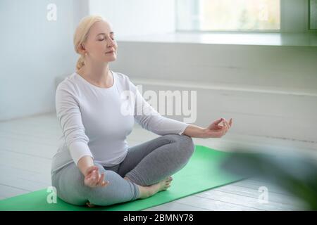 Reife blonde Frau sitzt in Lotushaltung, meditieren Stockfoto
