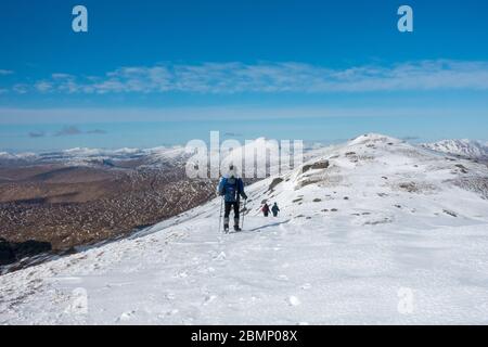 3 männliche Wanderer steigen vom Gipfelkairn des Ben Vorlich, einem munro im schottischen Hochland, ab. Ben Lui ist der weit entfernte Gipfel Stockfoto