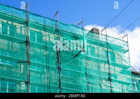 Grünes Sicherheitsnetz auf Gerüsten an der Fassade eines Mehrfamilienhauses Stockfoto