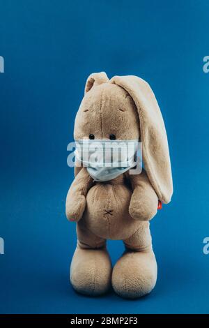 Spielzeughasen stehen in einer medizinischen Maske auf blauem Hintergrund. Konzept des Schutzes vor Atemwegserkrankungen, Viren und individuellen Atemschutzmaßnahmen. Coronavirus stoppen. Stockfoto