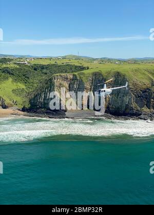 Dieser Hubschrauber fliegt tief über der Küste entlang des Strandes, so dass die Passagiere die wilden Tiere im Wasser besser sehen können. Stockfoto