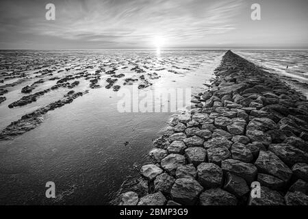 Schlammflat des 'waddenzee' bei Ebbe unter szenischem, dramatischem Sonnenuntergangshimmel mit Wolken Stockfoto