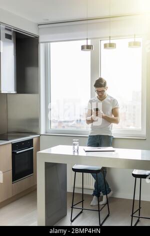 Gut aussehender Mann SMS mit seinem Smartphone in Küche Stockfoto