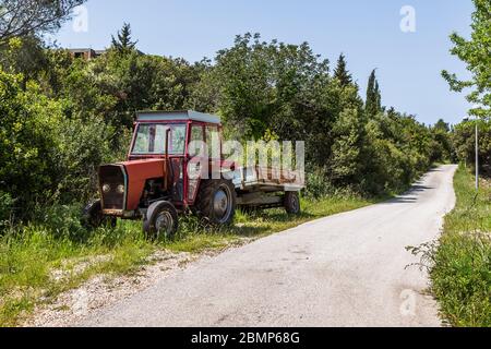 Alte rote Traktor auf Sipan Island auf der Seite einer Straße geparkt. Stockfoto