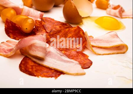 Zerbrochenes Hühnereier, Scheiben Wurst und Speck und Tomaten auf weißem Hintergrund. Nahaufnahme Stockfoto