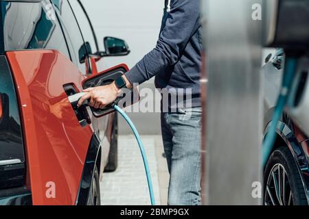 Der Mann lädt das Elektroauto an der Ladestation auf Stockfoto