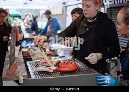 Eine Frau, die Wurst zum Verkauf auf dem Maltby Street Market in London grilt. Stockfoto