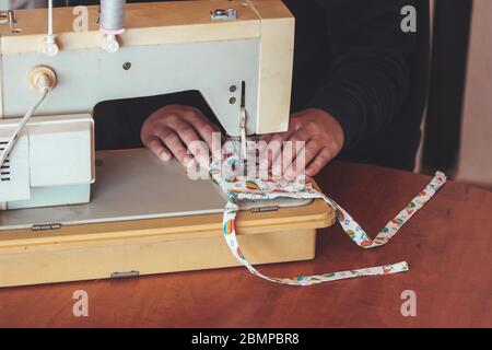 Frau händigt während der Coronavirus-Pandemie mit der Nähmaschine eine bunte Gesichtsmaske aus. Selbstgemachte Schutzmaske gegen den Virus. Nähmasken, COVID-19. Selektiver Fokus. Stockfoto