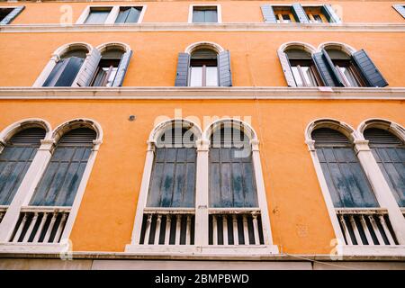 Hohe Bogenfenster in einem orangefarbenen Hochhaus in Venedig, Italien. Blaue Holzläden an alten Holzfenstern. Stockfoto