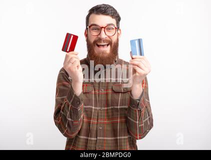 Aufgeregt bärtigen Mann hält zwei Kredit-oder Debitkarten über weißem Hintergrund. Stockfoto