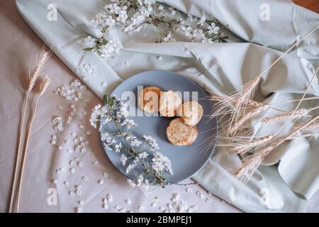 Frühstück am Morgen, getoastete schöne Käsekuchen auf einem Teller auf der Tischdecke neben einem Frühlingsstrauß aus weißen Blumen Stockfoto