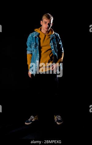 Trendy jungen Mann in sportlicher Jacke posiert in modernen Studio gegen schwarze Wand gekleidet Stockfoto