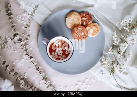 Frühstück am Morgen, getoastete schöne Käsekuchen auf einem Teller auf der Tischdecke neben einem Frühlingsstrauß aus weißen Blumen Stockfoto
