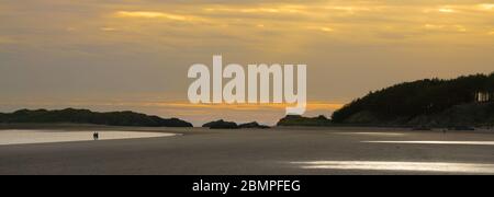 Panorama der Landschaft des britischen Strandes bei Sonnenuntergang. Ein Paar in Silhouette am Abend am Strand spazieren. Llanddwyn Island, Wales. Konzept Ruhe, Isolation. Stockfoto