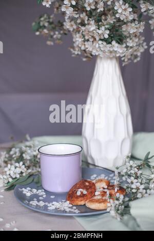 Frühstück am Morgen, getoastete schöne Käsekuchen auf einem Teller auf der Tischdecke neben einem Frühlingsstrauß aus weißen Blumen Stockfoto
