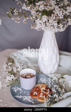 Frühstück am Morgen, getoastete schöne Käsekuchen auf einem Teller auf der Tischdecke neben einem Frühlingsstrauß aus weißen Blumen Stockfoto