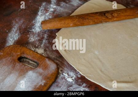 Dünn gerollter Teig für Fleischknödel auf dem Küchentisch. Ein Holznadel und ein Schneideglanz sind in der Nähe. Der Prozess der Zubereitung von hausgemachten Speisen Stockfoto