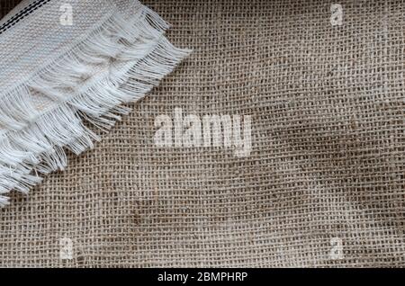 Stoffserviette mit Fransen auf Burlap. Leinenserviette in Weiß auf grobem Stoff. Multitasking Hintergrund aus natürlichen Stoffen. Blick von oben. Platz für Stockfoto