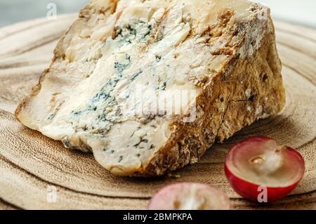 Ein Stück blauen Stilton Käse auf einem hölzernen antiken Hintergrund mit großen roten Trauben. Nahaufnahme. Stockfoto