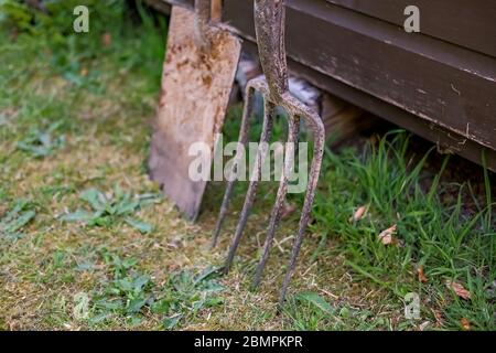 31 Gartengabel und Spaten lehnen sich gegen einen Holzschuppen mit selektivem Fokus auf die Gabel und absichtlich geringer Schärfentiefe Stockfoto