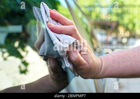 Eine Frau trocknet Autofenster mit einem alten Tuch, nachdem sie es gewaschen hat. Trocknen von Wasser in einem kürzlich gewaschenen Auto mit einem Tuch. Nahaufnahme der Hand der Frau. Stockfoto