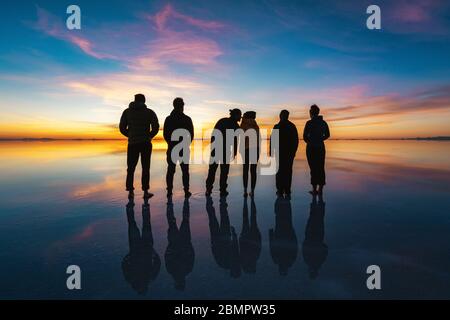 Gruppe junger Reisender, die den Sonnenaufgang in den Uyuni Salt Flats (spanisch: Salar de Uyuni) in Bolivien, Südamerika, beobachten. Stockfoto