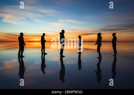 Silhouette junger Touristen gegen Sonnenaufgang in Uyuni Salt Flats (spanisch: Salar de Uyuni ) in Bolivien, Südamerika. Stockfoto