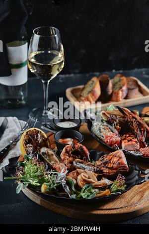 Frische Meeresfrüchte und Weißwein auf einem Steintisch. Austern, Garnelen und Jakobsmuscheln, Tintenfische, serviert vom Küchenchef, wunderschön auf Tellern, dunklem Beton Stockfoto