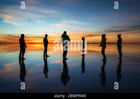 Silhouette junger Touristen gegen Sonnenaufgang in Uyuni Salt Flats (spanisch: Salar de Uyuni ) in Bolivien, Südamerika. Stockfoto