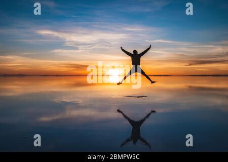 Junger Reisender, der gegen Sonnenaufgang in Uyuni Salt Flats (Spanisch: Salar de Uyuni) in Bolivien, Südamerika springt. Stockfoto