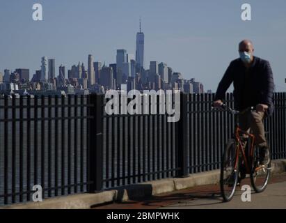 Hoboken, Vereinigte Staaten Von Amerika. Mai 2020. Ein Mann trägt eine schützende Gesichtsmaske, während er am Sonntag, den 10. Mai 2020, in Hoboken, New Jersey, mit Blick auf das One World Trade Center und die Skyline von Manhattan Fahrrad fährt. Die Coronavirus-Pandemie hat in New York City 20,000 Menschen getötet und weltweit über 270 00 Todesfälle. Foto von John Angelillo/UPI Quelle: UPI/Alamy Live News Stockfoto